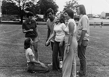 black and white photo of a group of male and female students on the athletic field
                              in the 1970s