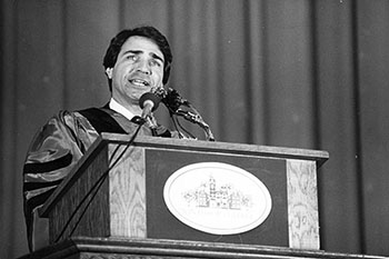 a black and white photo of Phil Lader speaking at a lectern in regalia