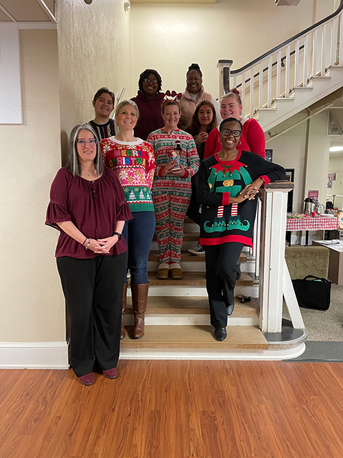 A group photo of Social Work faculty and students wearing Christmas sweaters on the
                        stairs in Bancroft Hall