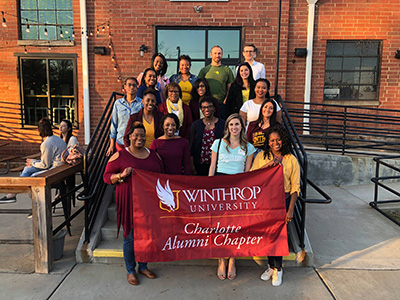 A group photo of Charlotte Alumni holding their chapter banner