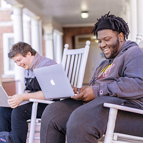 two students smiling while working on their laptops