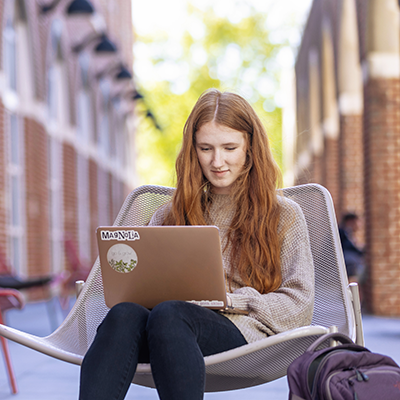 Woman with red hair sitting outside working on her laptop