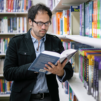 A man standing in a library reading a book