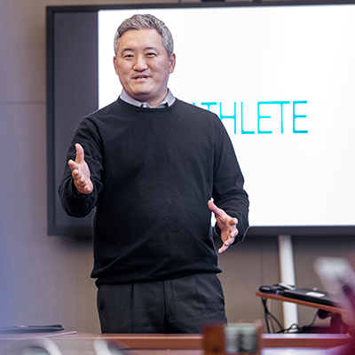 Man presenting in front of a large presentation screen with the word 