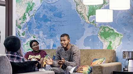 Students sitting on a couch and talking in front of a large world map