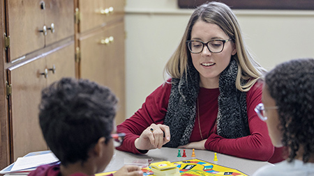 A student playing a board game with two young children