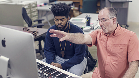 A student and professor working in the music computer lab